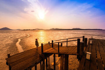 Person stands on a wooden pier watching a beautiful sunset over a tranquil coastal landscape