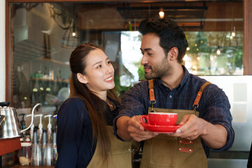 A couple of an Indian man and an Asian woman own a bakery together. holding a cup of red coffee stretched forward to deliver to customers who come to use the service in the cafe
