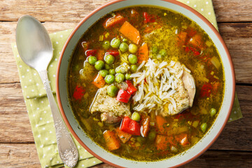 Peruvian cilantro chicken soup or Aguadito de Pollo with rice and vegetables closeup on the bowl on the wooden table. Horizontal top view from above