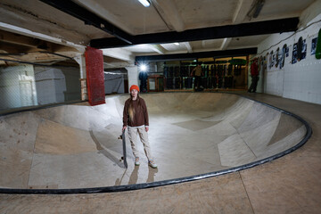 Young Caucasian woman wearing comfortable casual clothes standing with skateboard in bowl in skatepark, copy space