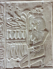 Wall bas relief of the Nile god Hapi shown kneeling holding an offering table loaded with...
