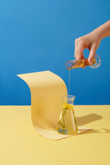 A female hand is pouring a liquid like calendula essence into a glass vase on a blue background....