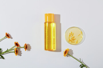 Scene for advertising and branding product with blank space on cosmetics bottle mockup. Petri dishes containing calendula flowers and essence decorated on a white background, top view