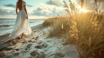 Woman in a white dress walking barefoot on sand at the beach next to reeds