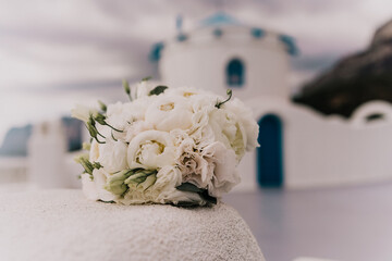 A bouquet of white flowers sits on a ledge next to a blue building. The flowers are arranged in a...