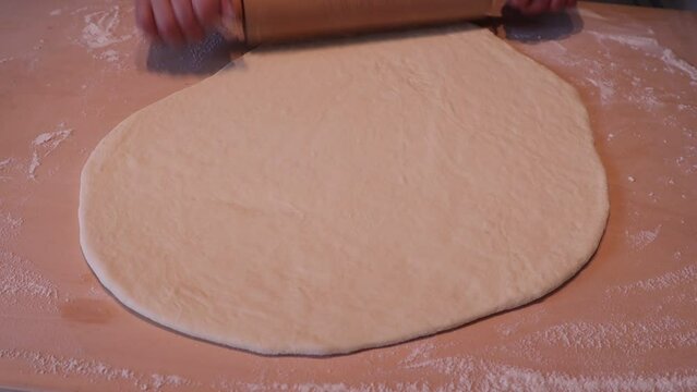 Woman using a wooden rolling-pin with dough in kitchen. Making Italian traditional Tigelle.