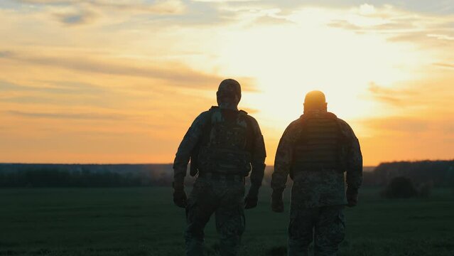 military men returning after completing a task. Soldiers in military uniform walk on a stony road