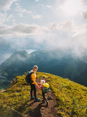 Mother and child with backpack hiking in mountains together summer family vacations in Norway...