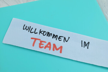 Concept of Willkommen Im Team write on sticky notes isolated on Wooden Table.