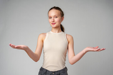 Young Clueless Woman Standing With Outstretched Arms on gray background