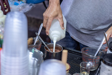 Male merchant is pouring milk into a bottle with coffee to mix it in an iced milk coffee menu, Cold milk coffee is a popular drink in Thailand