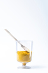 Colorful yellow holi powder sand in a glass cup with wooden spoon on white background.