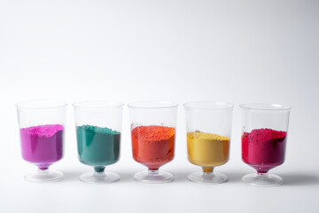 Multicolored holi powder sand in measuring cup row isolated on white background.