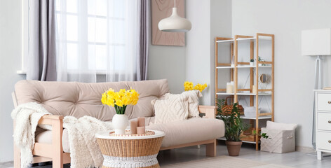 Stylish living room with comfortable sofa, coffee table and bouquet of narcissus flowers