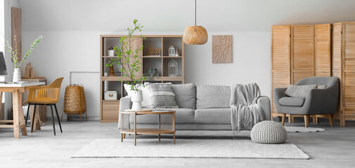 Interior of stylish living room with cozy sofa, coffee table and blooming tree branches in vase