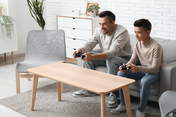 Father and his little son playing video games on sofa at home