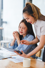 Two engaged businesswomen using a tablet and discussing work with focus and interest at an office desk.