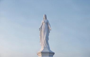 A front-facing view of the compassionate Our Lady, Mother of Jesus Christ (also known as Madonna or Mother Mary in the Christian religion), against a clear sky during the golden hour.
