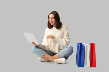 Young woman with laptop and shopping bags on white background