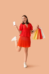 Young woman with credit card, mobile phone and shopping bags on beige background