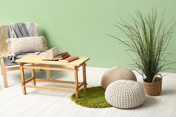 Coffee table with poufs, chair and houseplant near green wall