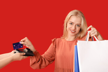 Woman with shopping bags paying for purchases via terminal on red background