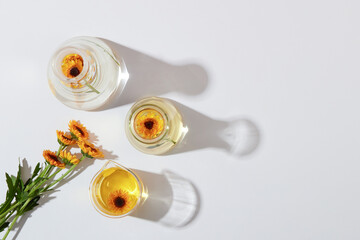 Mockup scene for cosmetic of calendula extract. Top view of fresh calendula flowers on lab glassware with essence decorated on a white background. Minimal concept, copy space