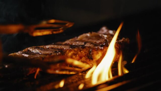 Person places piece of meat onto a hot grill and turns it over