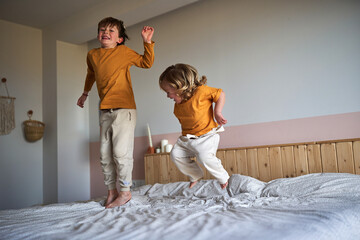 Siblings playing and jumping on parents bedroom