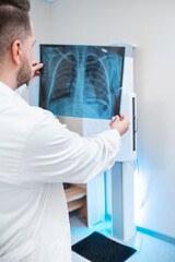 male doctor examines pictures of the lungs and ribs in the x-ray room, in the background x ray machine