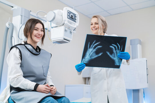 a female doctor and a young female patient look at an x-ray of hands, fingers and rejoice in the radiology room against the background of medical equipment. No bone fracture.	