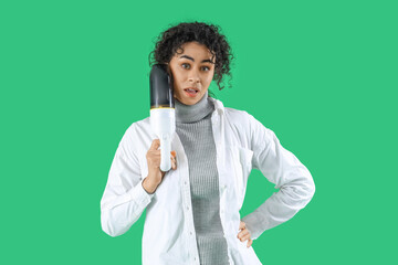Shocked young African-American woman with handy vacuum cleaner on green background
