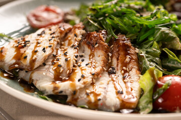 Green salad with smoked eel fish, avocado slices and chuka seaweed, close-up. Japanese cuisine concept.