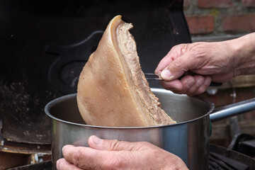 Cook takes a piece of slowly cooked rind meat out of the pot to make a stock sauce in a rustic kitchen, copy space, selected focus