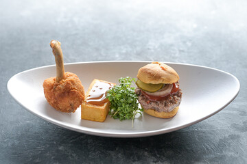 Traditional fast food served as a gourmet dish of a chicken drumstick, fried potato square with ketchup and a mini burger on a white plate, copy space, selected focus