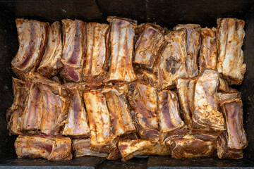 Seasoned and marinated beef short ribs are placed in a large black metal bowl, preparation for a barbecue party with many guests, top view from above