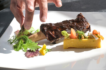 chef arranging salad for the finishing touch on a gourmet dish with short rib, polenta and...