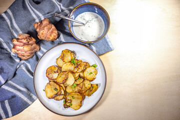 Fried slices of Jerusalem artichoke or topinambur (Helianthus tuberosus) with onions, parsley garnish and a yogurt dip, healthy root vegetable, copy space, top view from above