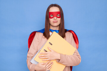 Sad upset woman wearing superhero costume and mask holding folders isolated over blue background...