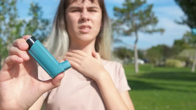 Irritated girl with allergy attack. A teen with inhaler stand in green nature and suffer from asthma symptoms.