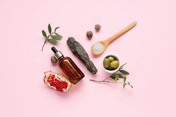 Beautiful composition with bottle of natural essential oil, olives and pomegranate on pink...