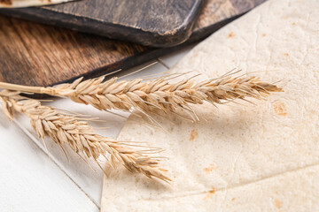 Ears of wheat and thin lavash on white wooden background, closeup