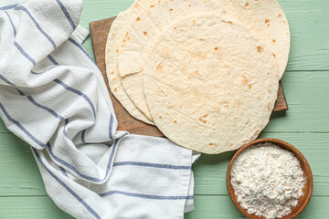 Tasty lavash, bowl with flour and napkin on green wooden background
