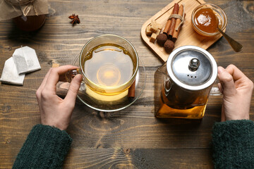 Female hands holding teapot and cup of fresh cinnamon tea on wooden background, closeup