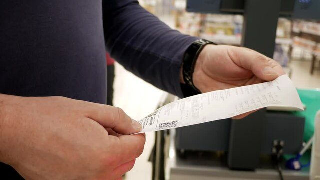 A man checks a receipt for paying for groceries in a store near the cash register. Shopping at the supermarket. Product prices. Close-up of a man's hands holding a paper receipt.
