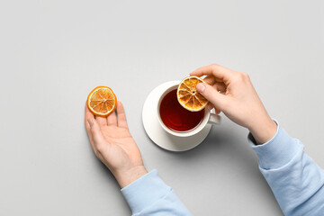 Female hands adding slices of dried orange in cup of black tea on light background