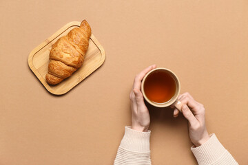 Female hands holding cup of tea and croissant on brown background