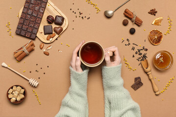 Female hands holding cup of black tea and sweets on brown background