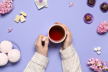 Female hands with cup of tea and candies on color background