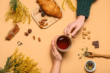 Female hands holding cup of tea, mimosa and croissant on color background